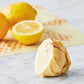 Lemons and a crumpled piece of paper on a marble surface with a tortilla in the background.