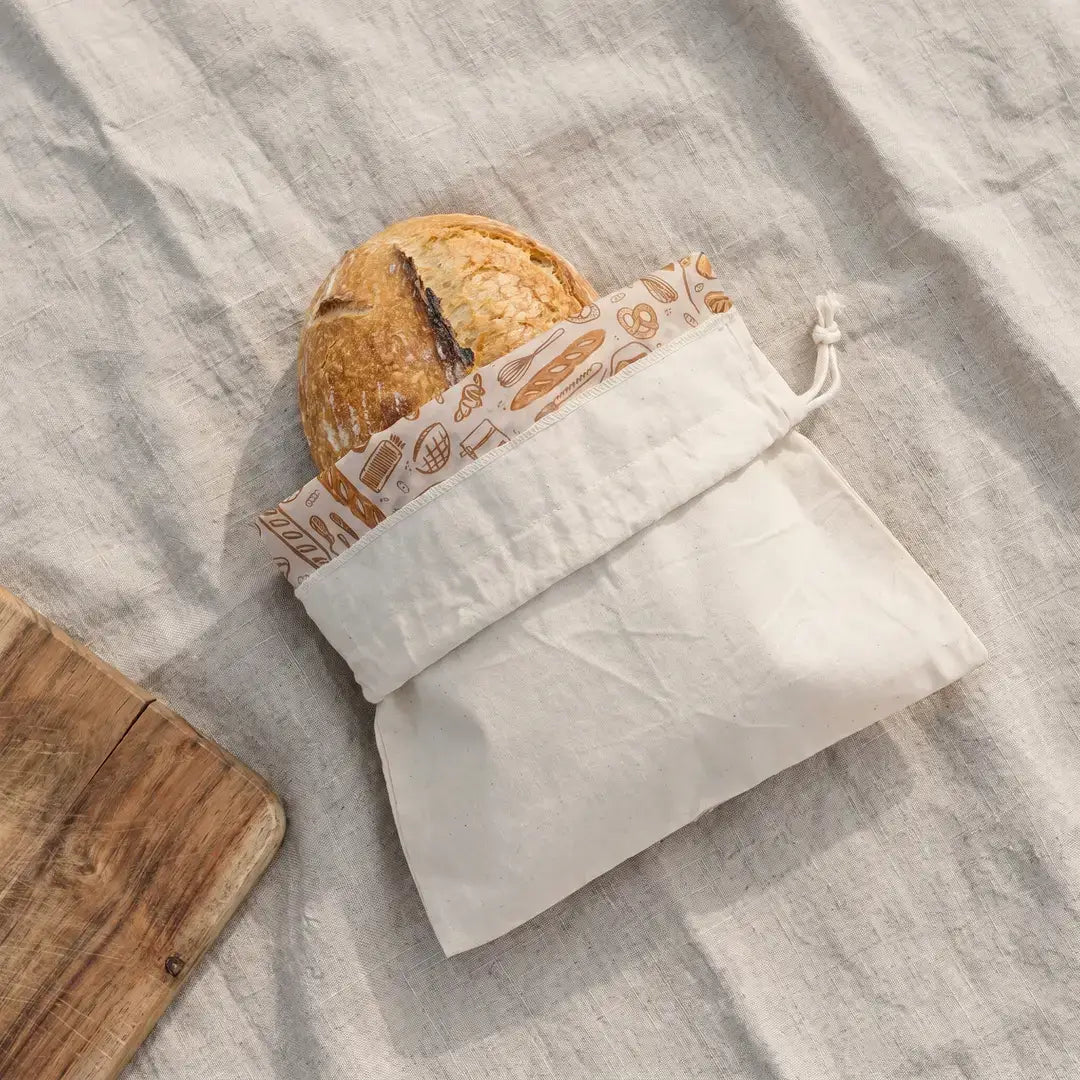 Loaf of bread in a white drawstring bag on a textured surface
