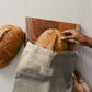 Person taking bread out of a reusable bag with a wooden cutting board and loaf of bread on a white surface.
