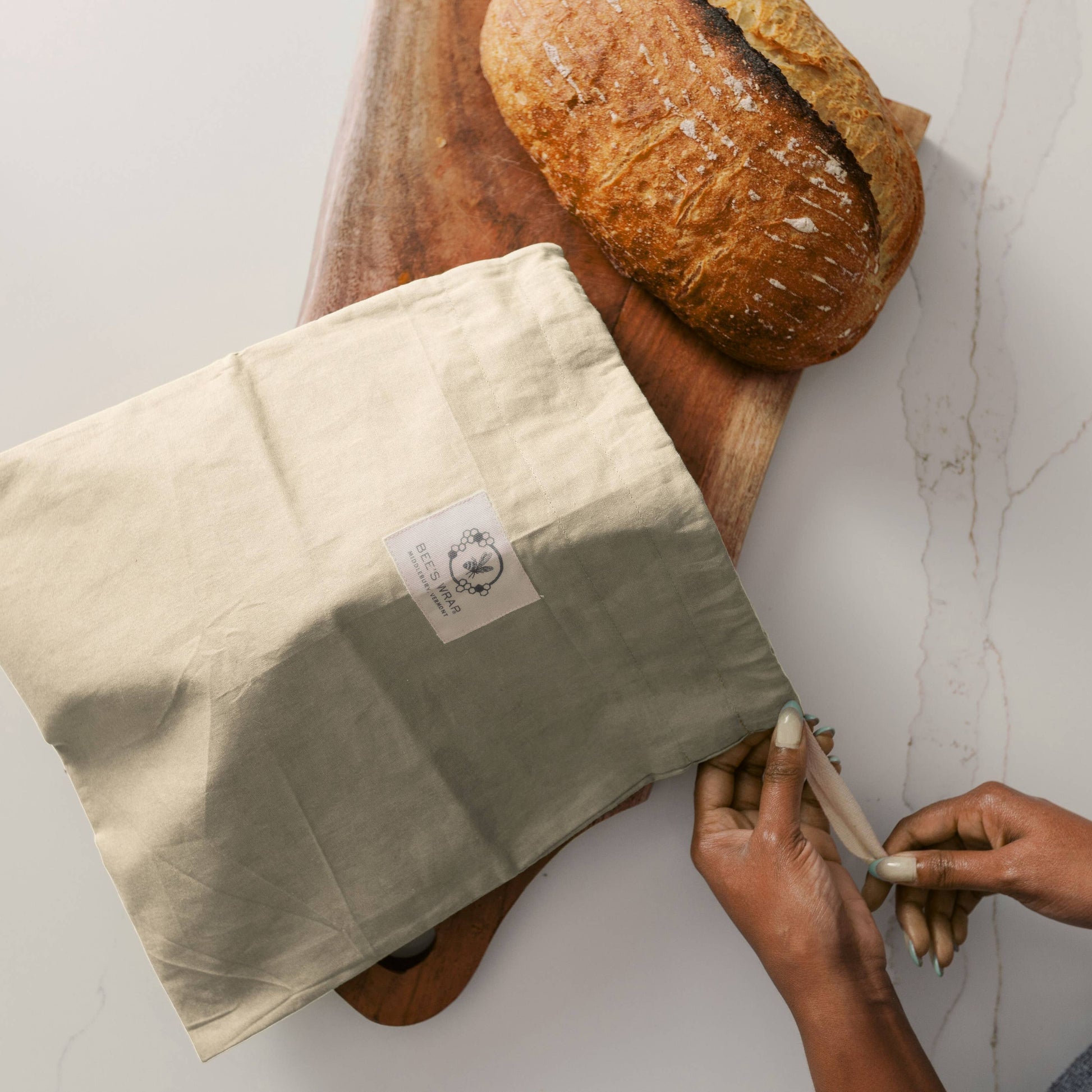 Person wrapping a loaf of bread in a cloth with a visible brand label on a white surface.