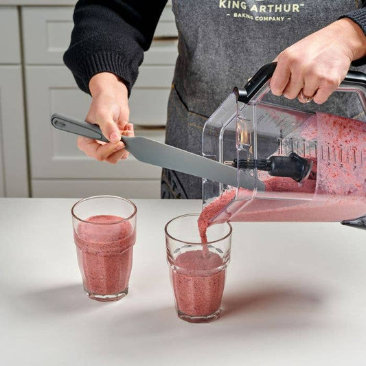 Person pouring a pink smoothie from a blender into two glasses.