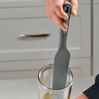 Person using a kitchen tool to mix ingredients in a container on a kitchen counter.