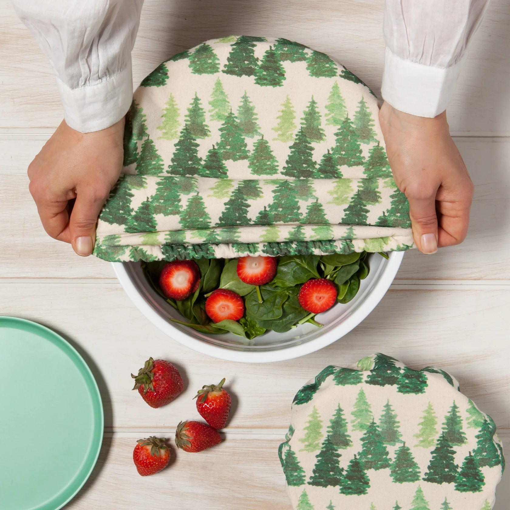 Reusable food wraps with tree pattern being used to cover a bowl of salad on a wooden surface.