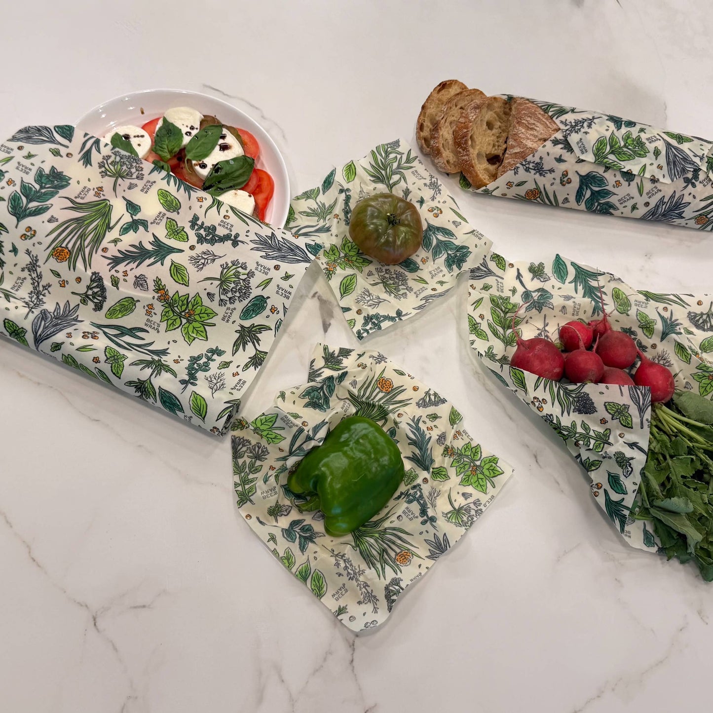 Set of floral-patterned beeswax wraps on a marble surface with fruits and vegetables.