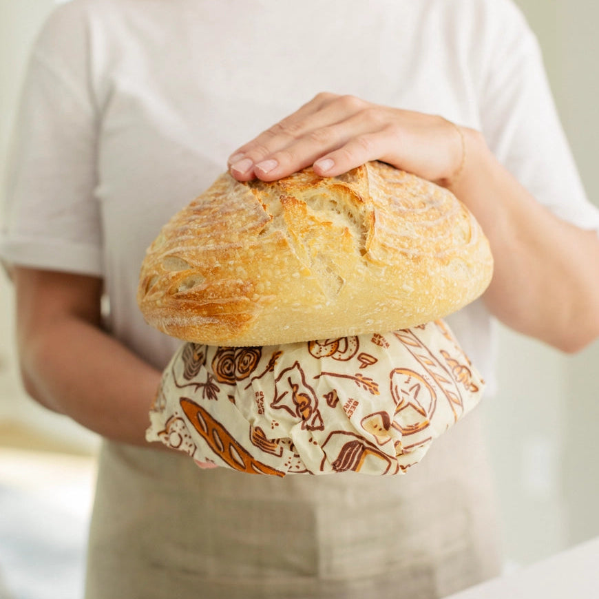 Person holding a loaf of bread wrapped in a patterned paper bag.