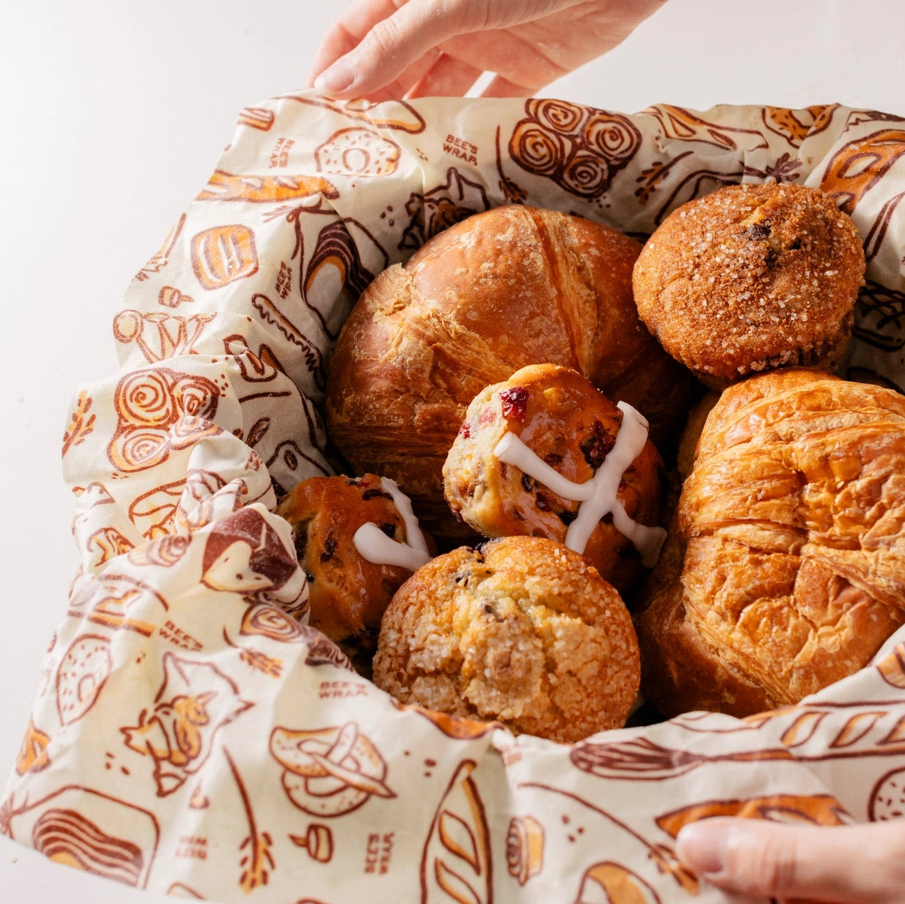 Basket of bread rolls with patterned paper lining, held by a person.
