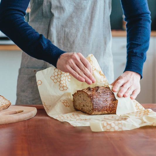 Person unwrapping a loaf of bread on a wooden table with a neutral background