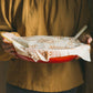 Person holding a red dish with a floral-patterned cloth over it