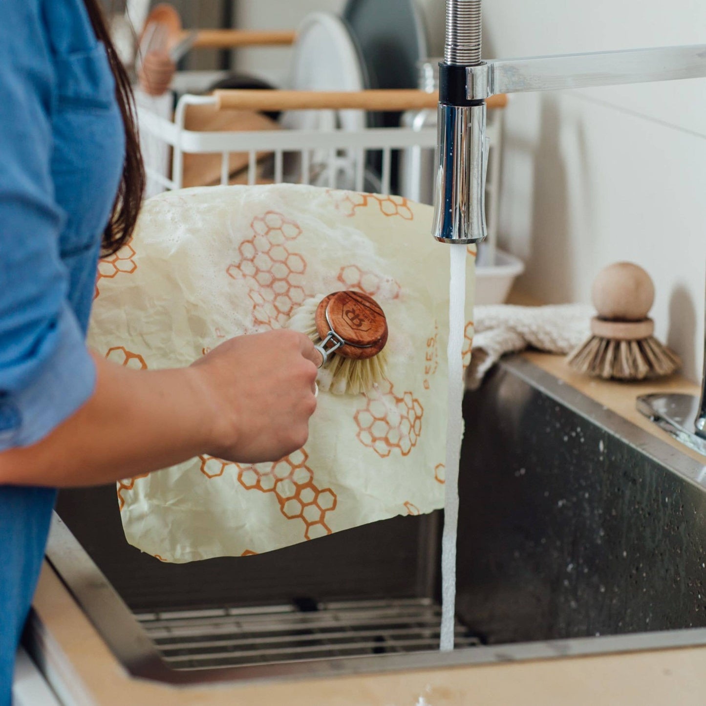 Person washing a wooden scrubber under running water in a kitchen sink.