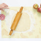 Person rolling out dough with a wooden rolling pin on a floured surface with apples nearby.