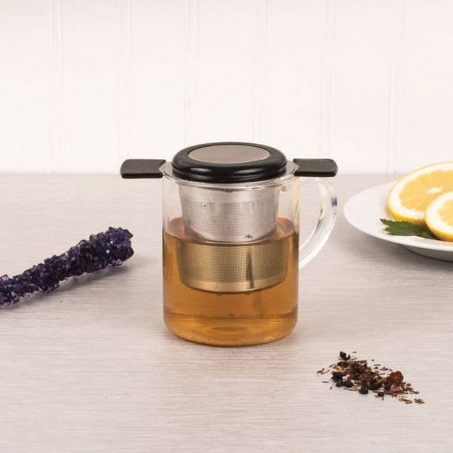 Glass teapot with metal infuser on a light surface with lavender and lemon slices.