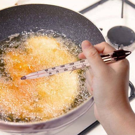 Frying food in a pan with a thermometer inserted, showing the temperature.