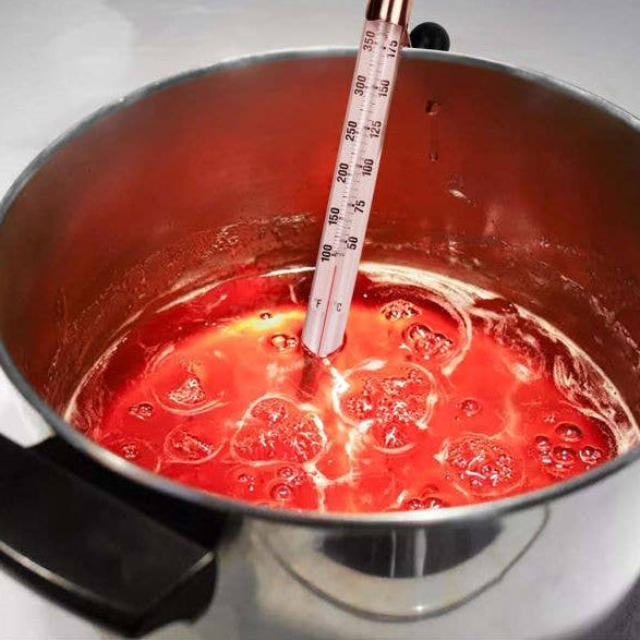 Red liquid being heated in a pot with a thermometer inside
