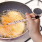 Frying food in a pan with a thermometer inserted, showing the temperature.