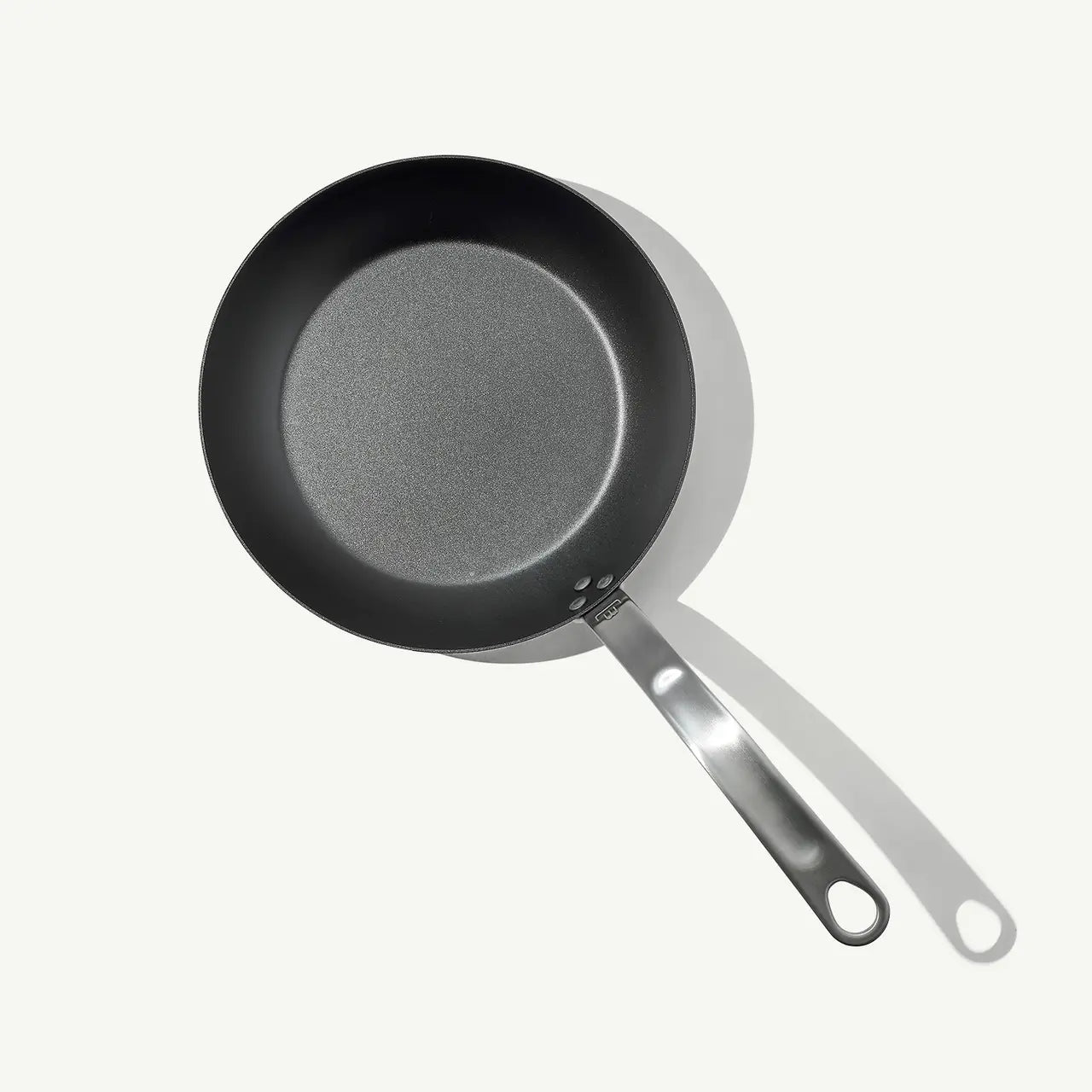 A black carbon steel frying pan with a stainless steel handle, pre-seasoned and ready for cooking.
