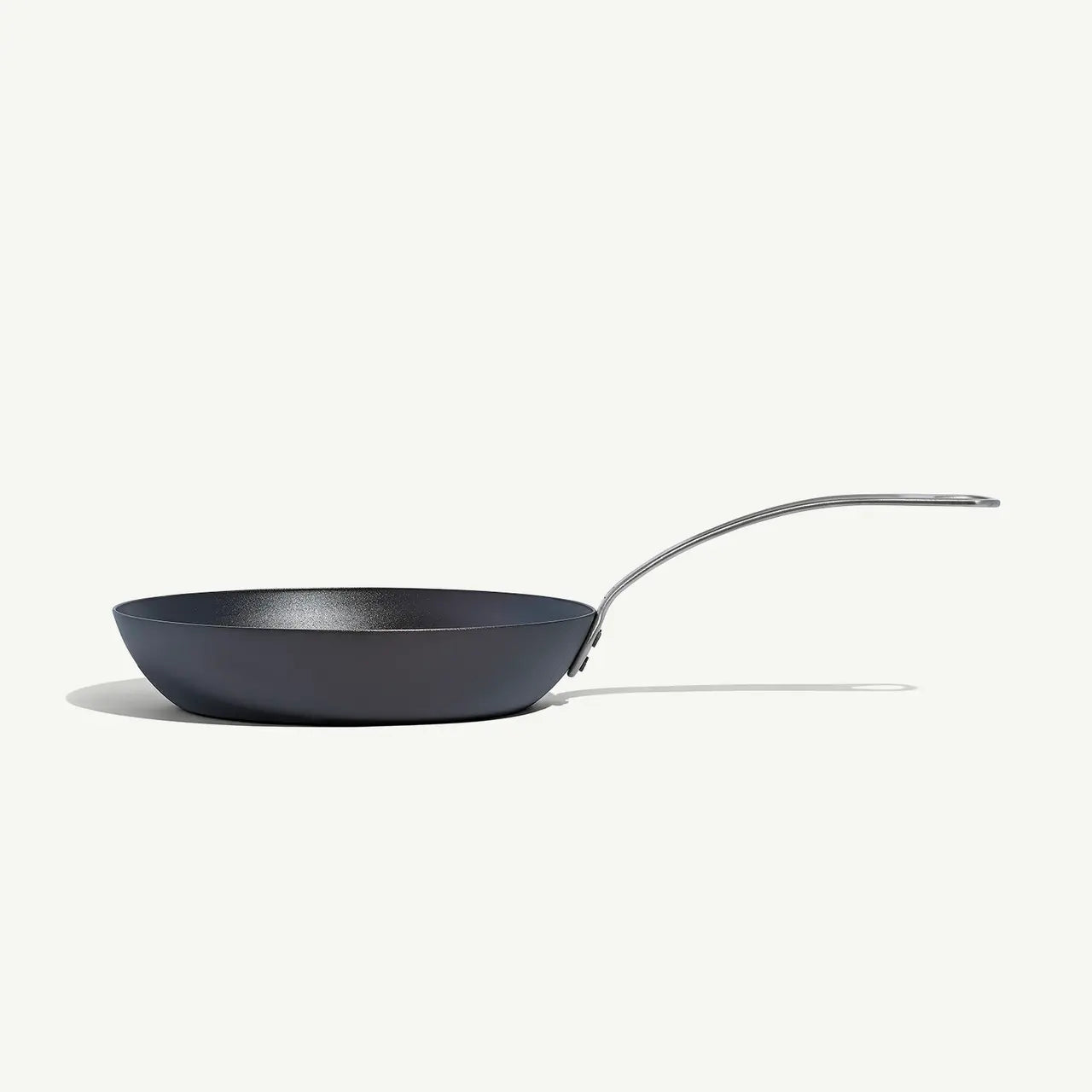 A black carbon steel frying pan with a stainless steel handle, pre-seasoned and ready for cooking on a white background.