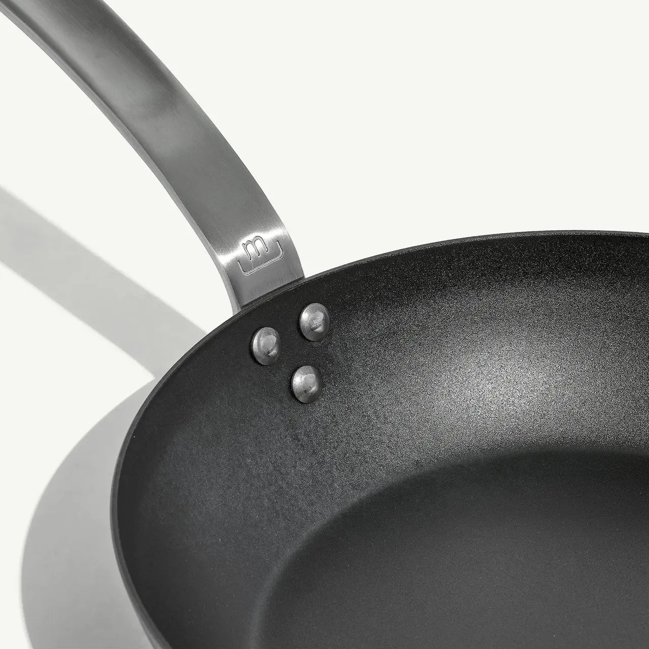 A black carbon steel frying pan with a stainless steel handle, pre-seasoned and ready for cooking on a white background.