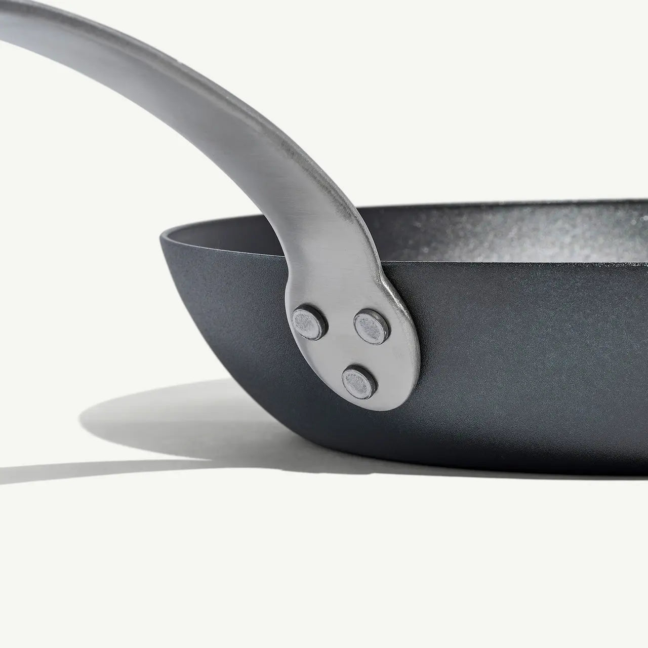 A black carbon steel frying pan with a stainless steel handle, pre-seasoned and ready for cooking on a white background.