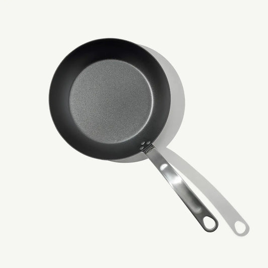 A black carbon steel frying pan with a stainless steel handle, pre-seasoned and ready for cooking.