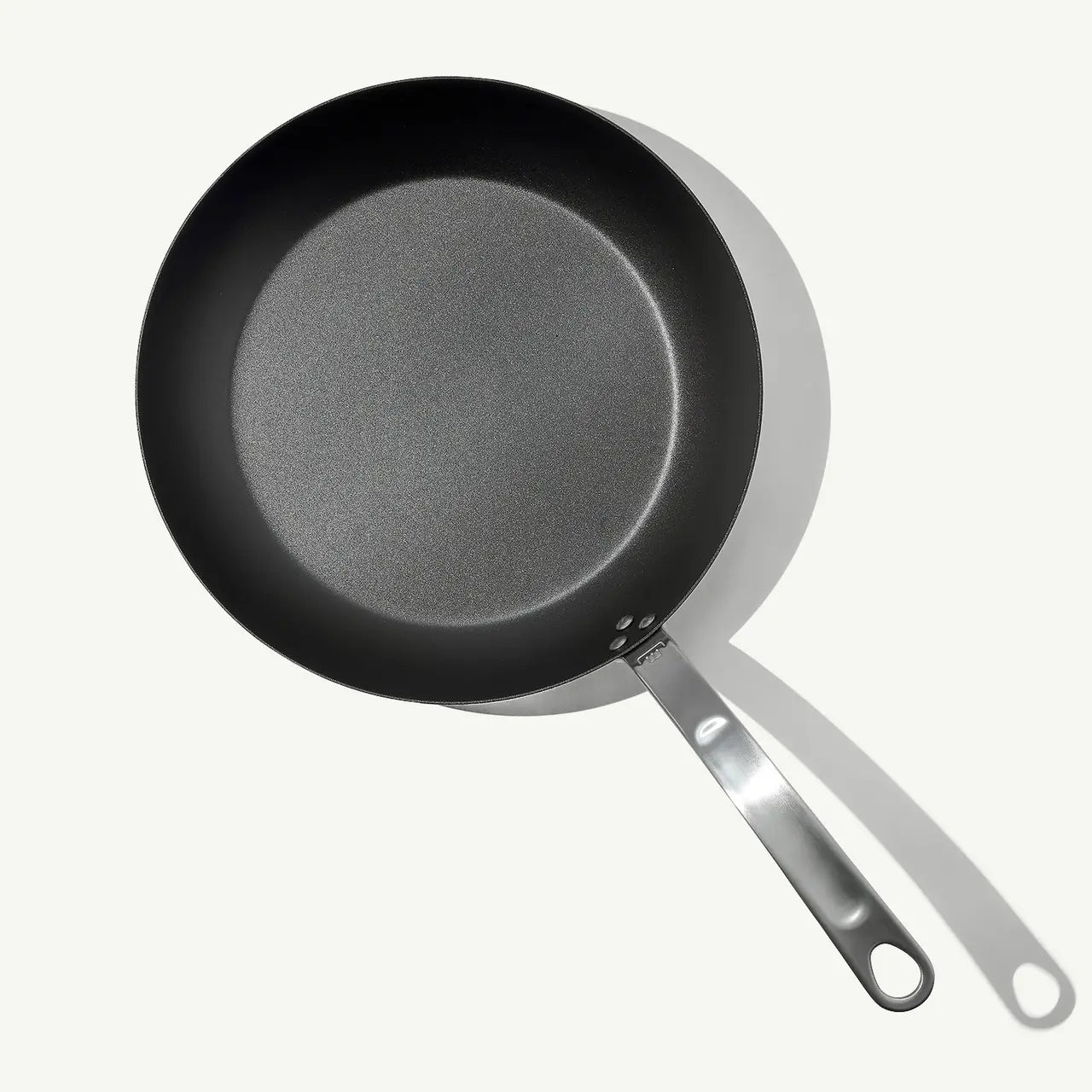 A black carbon steel frying pan with a stainless steel handle, pre-seasoned and ready for use on white background.