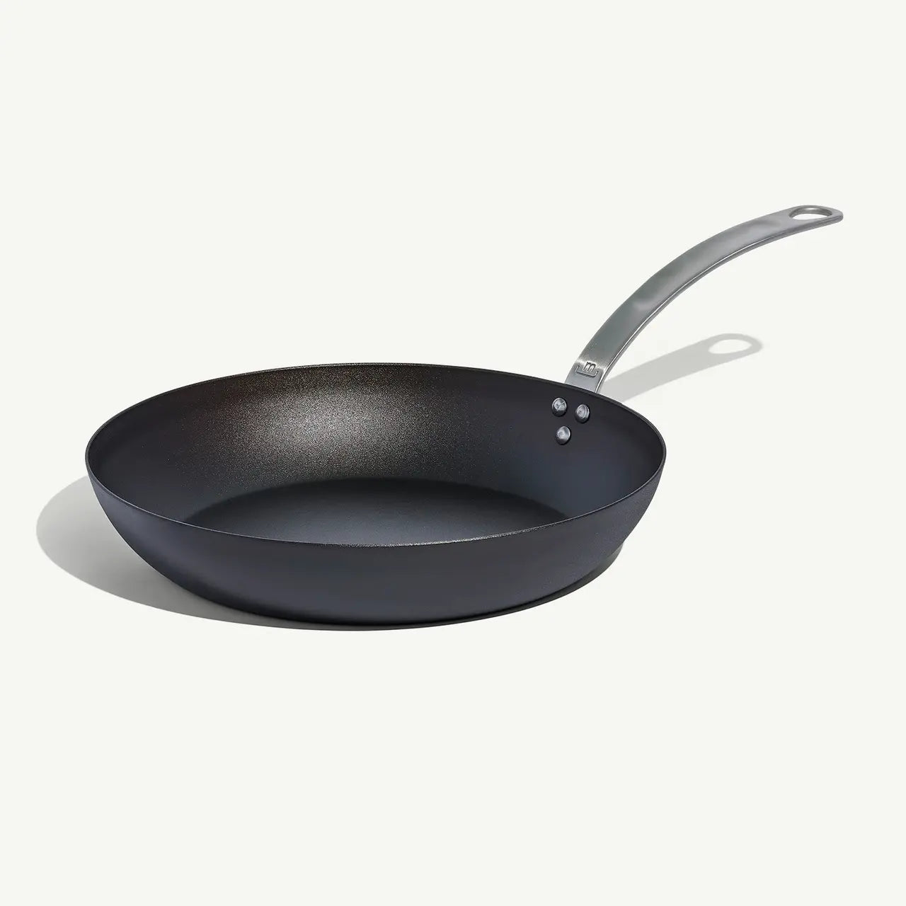 A black carbon steel frying pan with a stainless steel handle, pre-seasoned and ready for use on white background.