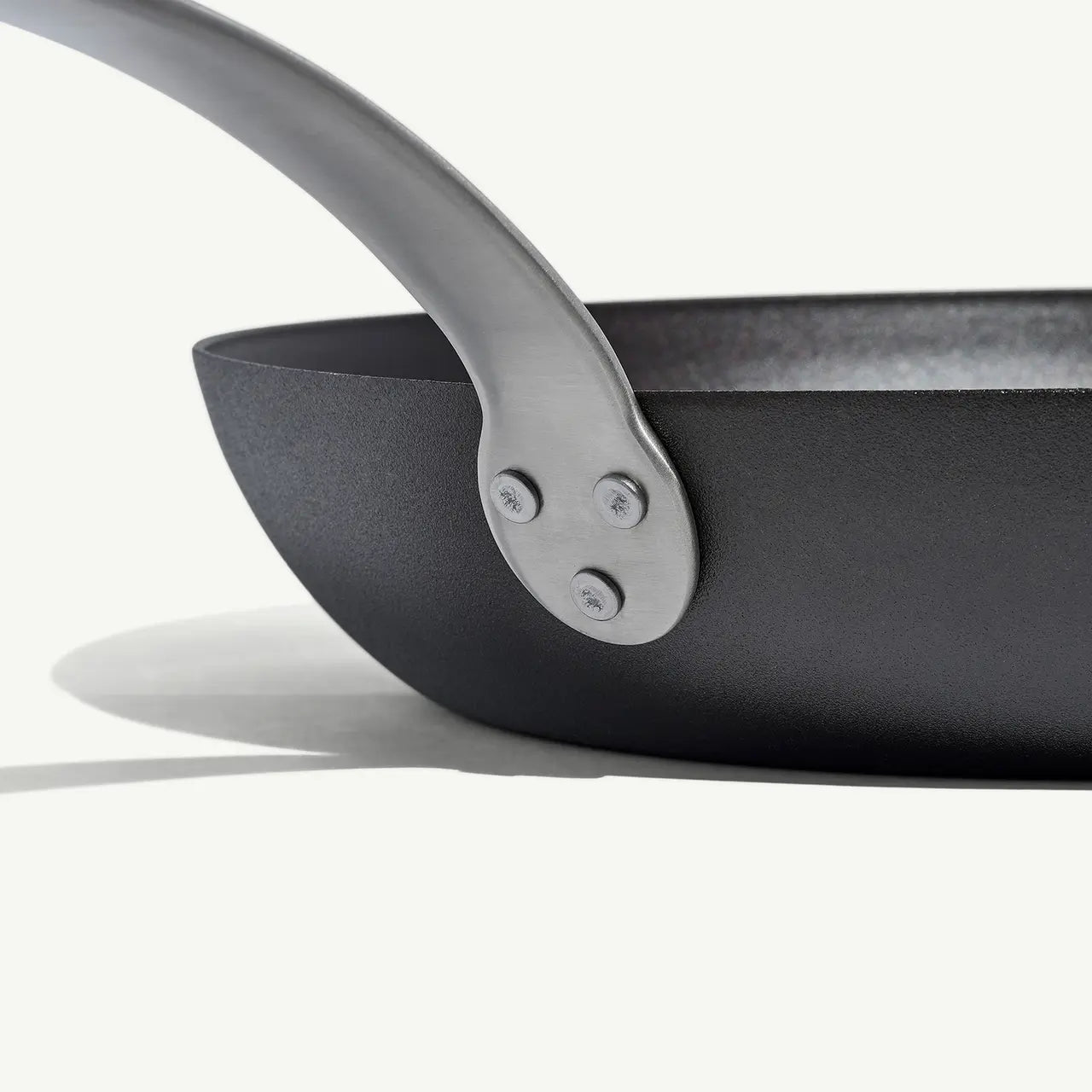 A black carbon steel frying pan with a stainless steel handle, pre-seasoned and ready for use on white background.