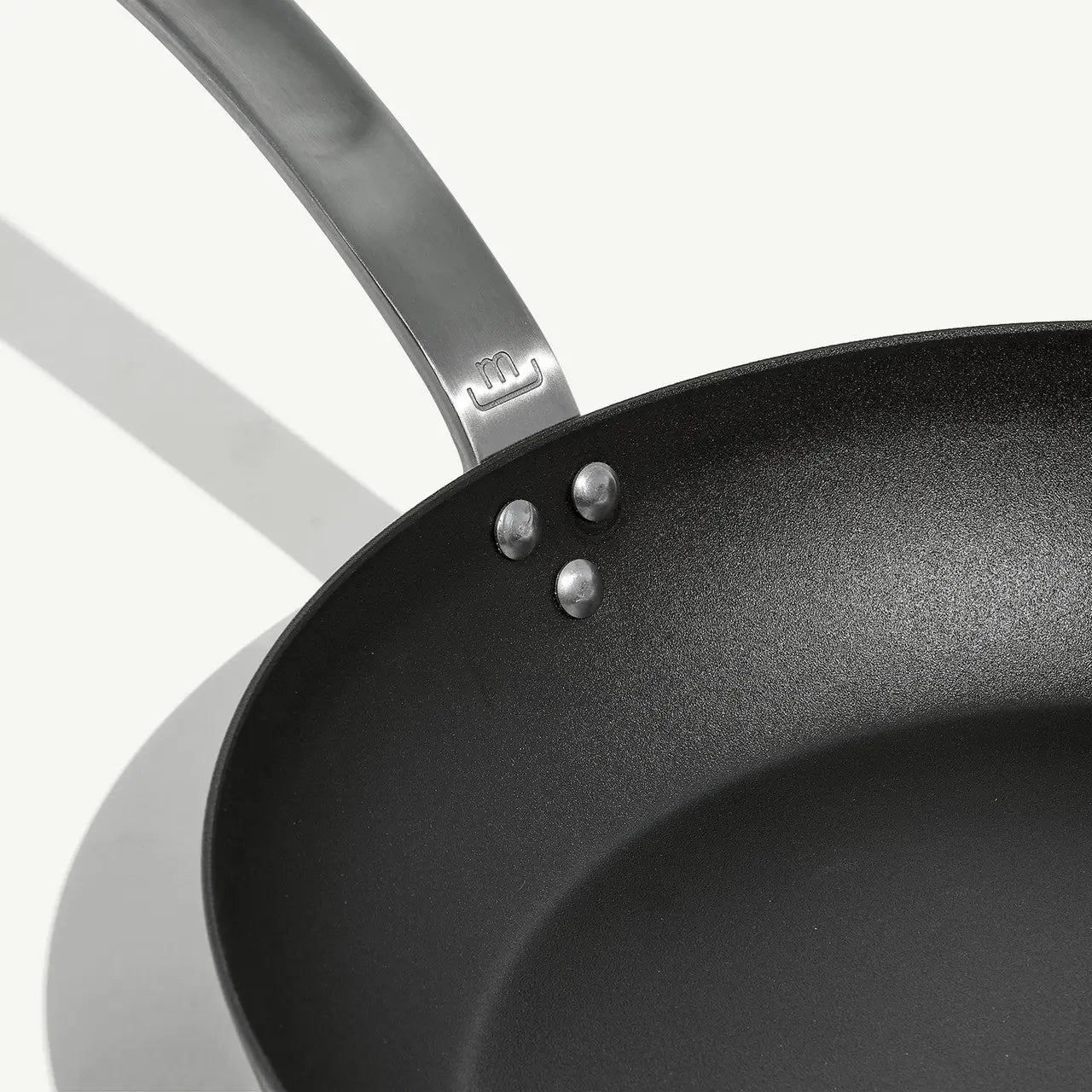 A black carbon steel frying pan with a stainless steel handle, pre-seasoned and ready for use on white background.