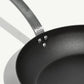 A black carbon steel frying pan with a stainless steel handle, pre-seasoned and ready for use on white background.