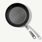 A black carbon steel frying pan with a stainless steel handle, pre-seasoned and ready for use on white background.