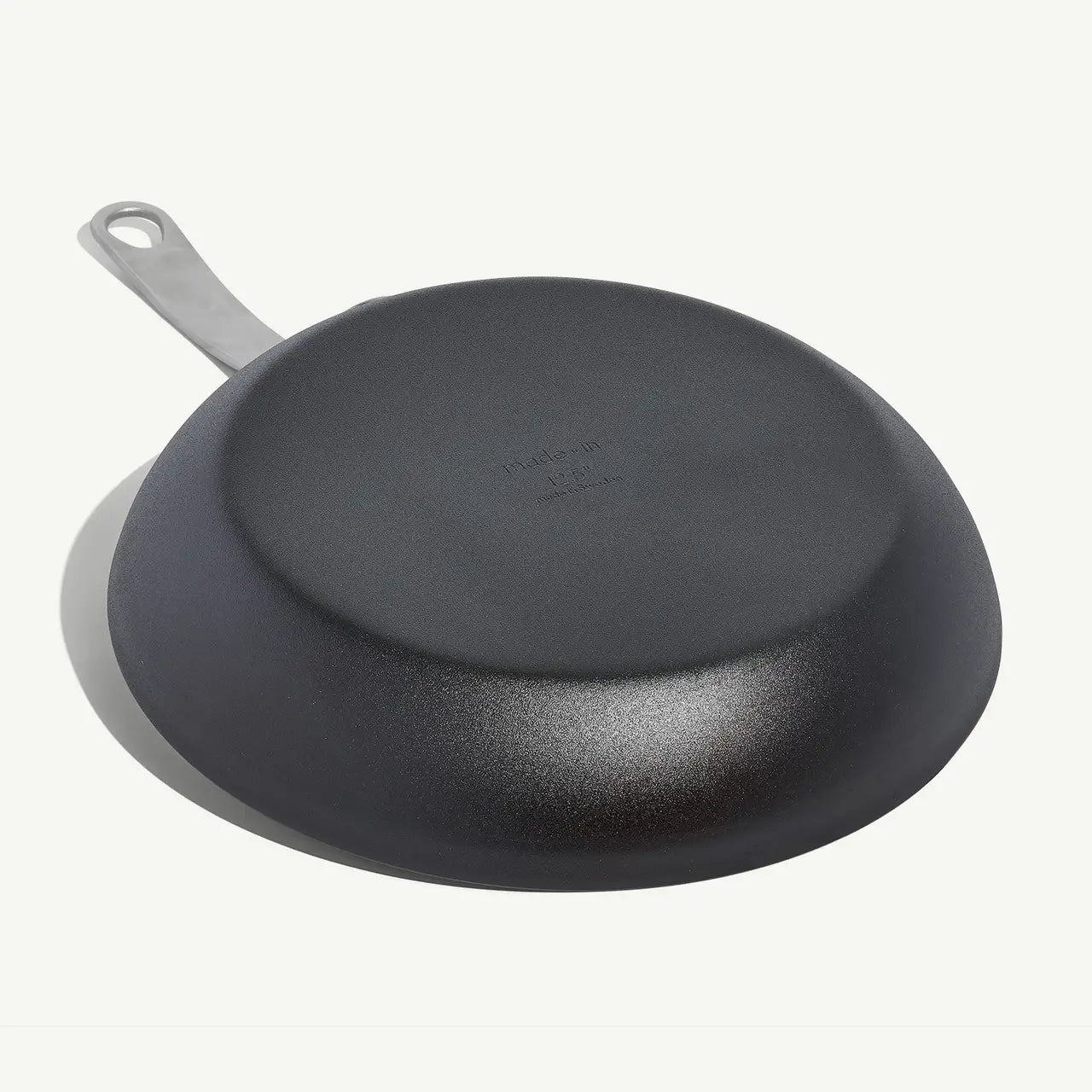 A black carbon steel frying pan with a stainless steel handle, pre-seasoned and ready for use on white background.