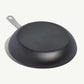 A black carbon steel frying pan with a stainless steel handle, pre-seasoned and ready for use on white background.