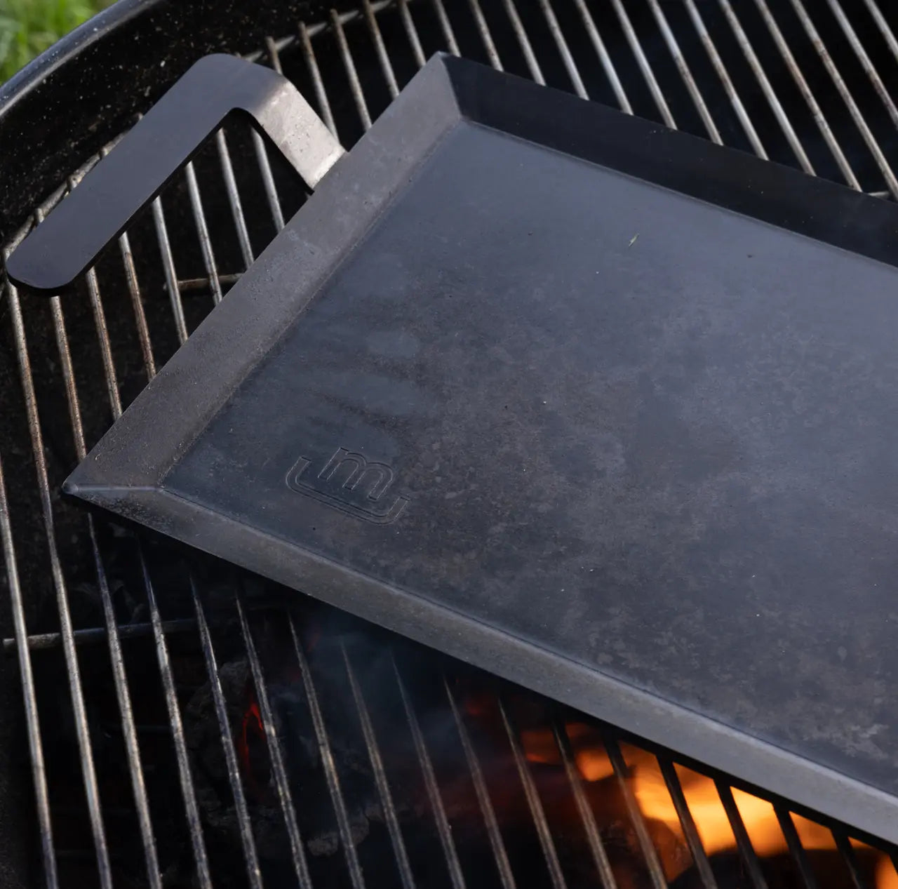 Black rectangular griddle on a grill outside. 