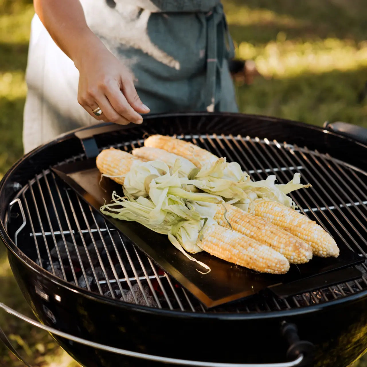 Black rectangular griddle on a grill outside with corn on the cob. 
