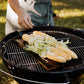 Black rectangular griddle on a grill outside with corn on the cob. 