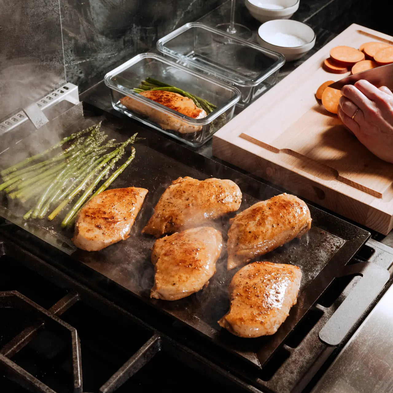 Cooking dinner items on a black griddle, chicken, asparagus. 