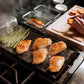 Cooking dinner items on a black griddle, chicken, asparagus. 