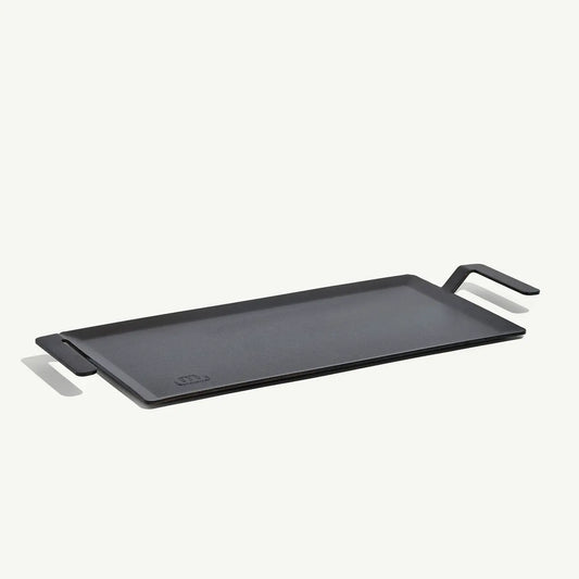 A black carbon steel griddle with raised handles, designed for use on stovetops and grills.