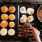 Cooking breakfast items on a griddle with pancakes, eggs, and bacon.