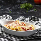 Bowl of pasta with cheese on a checkered cloth with tomatoes in the background