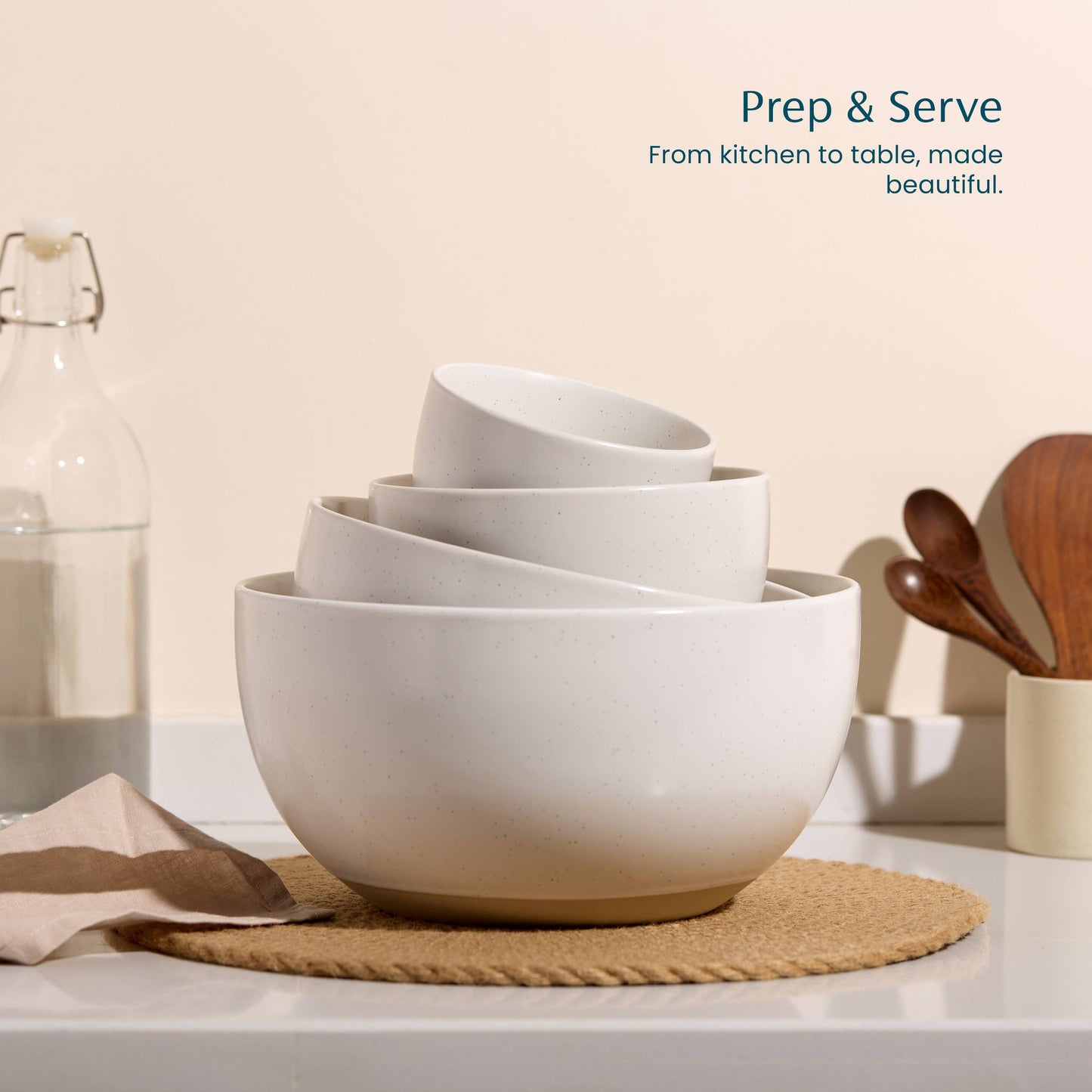 White ceramic bowls stacked on a kitchen counter with wooden utensils and a bottle in the background.