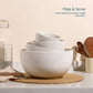 White ceramic bowls stacked on a kitchen counter with wooden utensils and a bottle in the background.