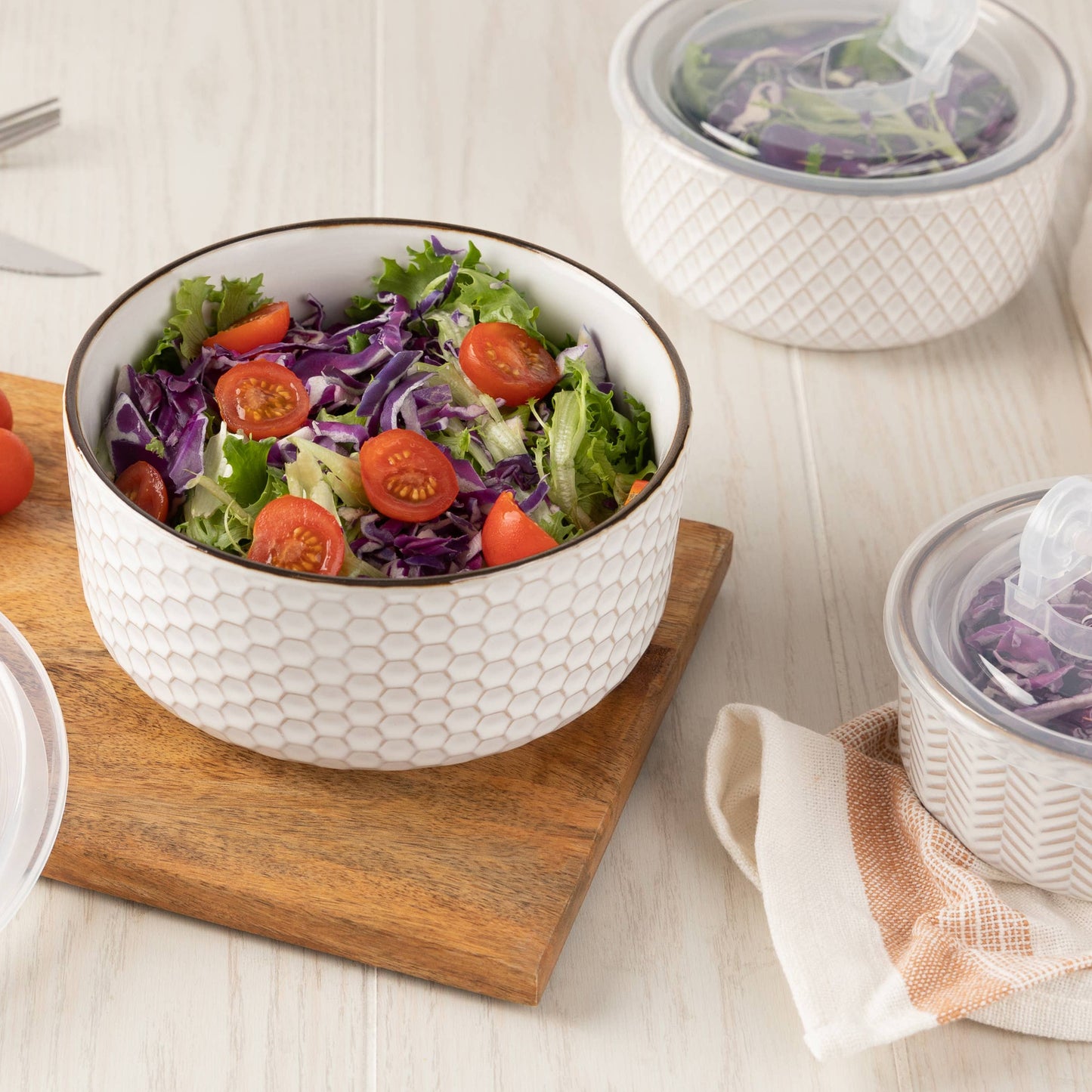White bowl with salad on a wooden cutting board, surrounded by cherry tomatoes and other containers.