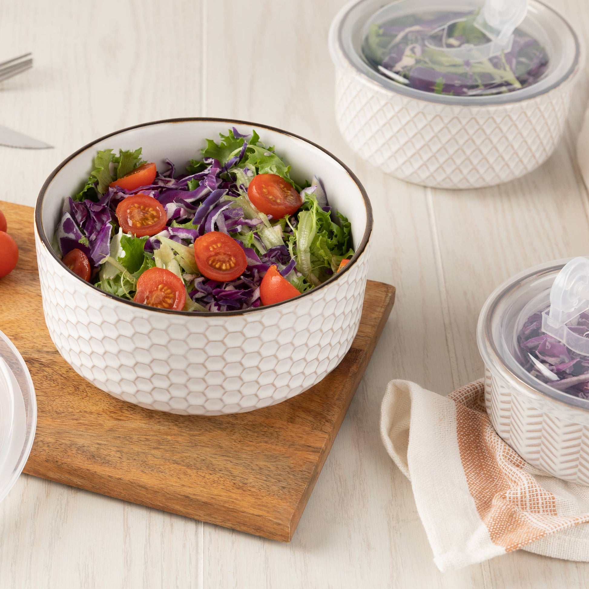 White bowl with salad on a wooden cutting board, surrounded by cherry tomatoes and other containers.