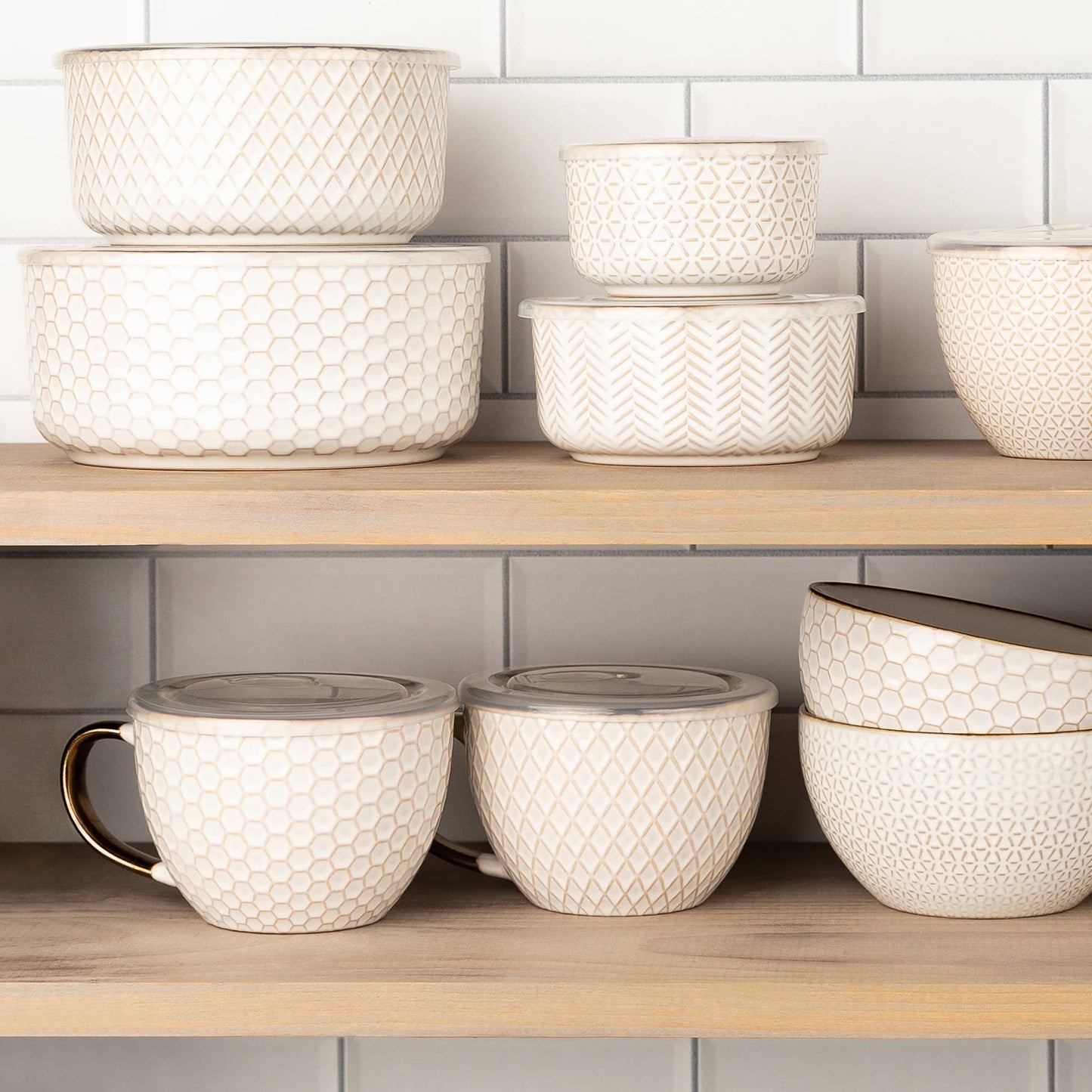 Set of ceramic bowls and mugs on a wooden shelf with a tiled wall background