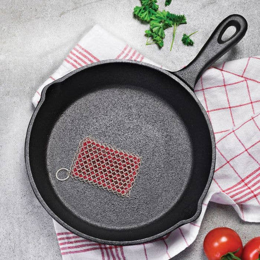 Cast iron skillet with a mesh scrubber on a gray surface with a checkered cloth.