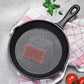 Cast iron skillet with a mesh scrubber on a gray surface with a checkered cloth.