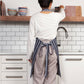 Person in a kitchen wearing an apron, standing by a shelf with bowls.