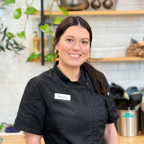 Woman wearing a black chef's coat with a name tag in a kitchen setting
