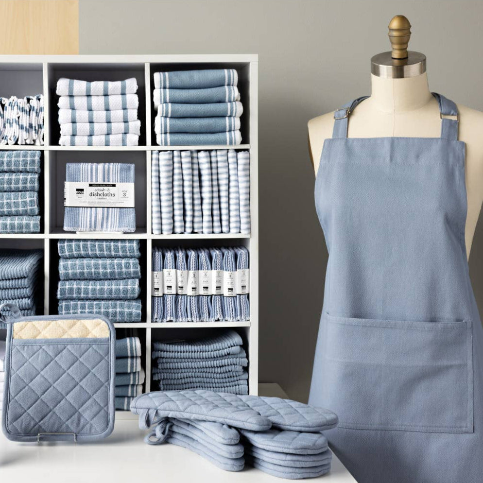 Set of blue kitchen towels, potholders, and an apron displayed on a mannequin against a gray wall.