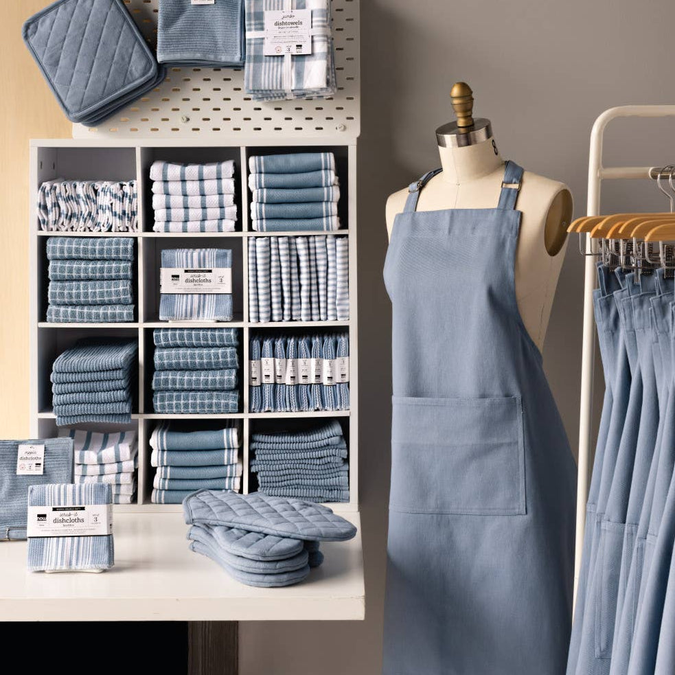 Display of blue kitchen towels, aprons, and pot holders in a store setting.